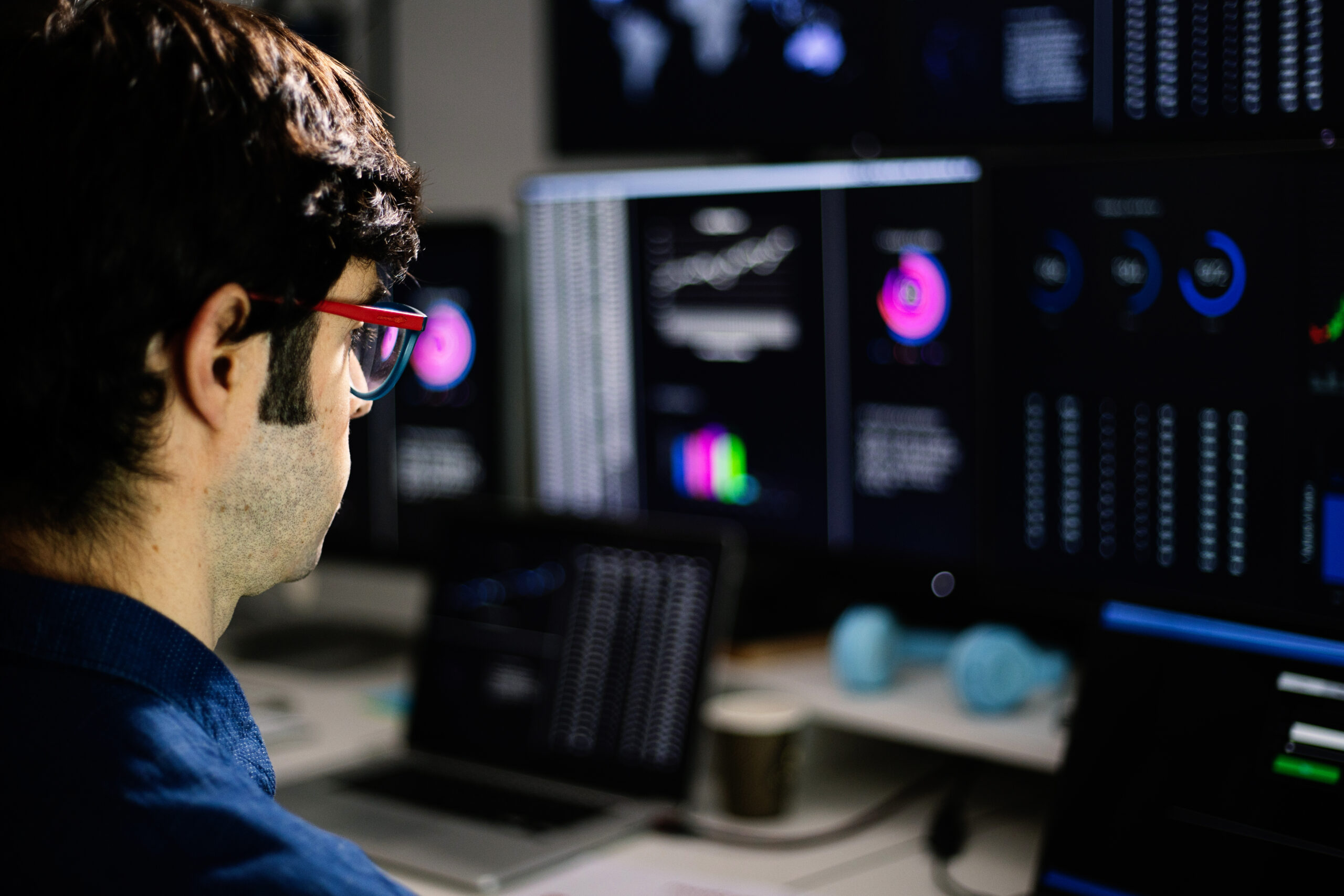 Stock trader analyzing charts on multiple computer screens in office at night